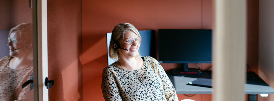 Veritaksen asiakaspalvelija hymyilee puhuessaan puhelimessa kuulokkeilla.