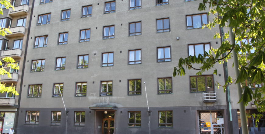 Foto av fasaden på Hesperiagatans flervåningshus. Huset har sex våningar och är grått. Vid ingången finns några trappor och dubbeldörrar.