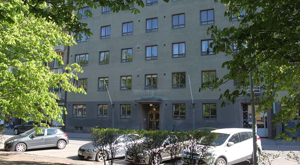 Foto av fasaden på Hesperiagatans flervåningshus med parkeringsplatser i förgrunden.