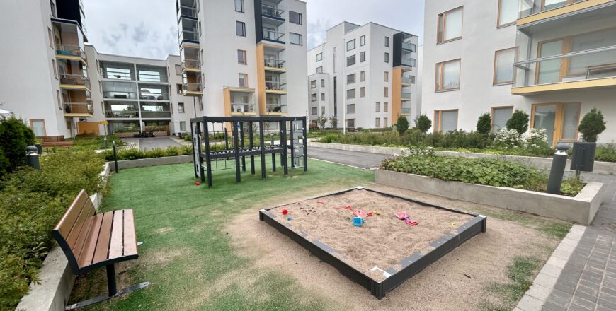 Flervåningshusen på Koltgränden fotograferad från gården. Det finns en sandlåda och klätterställning samt en bänkar på gården.