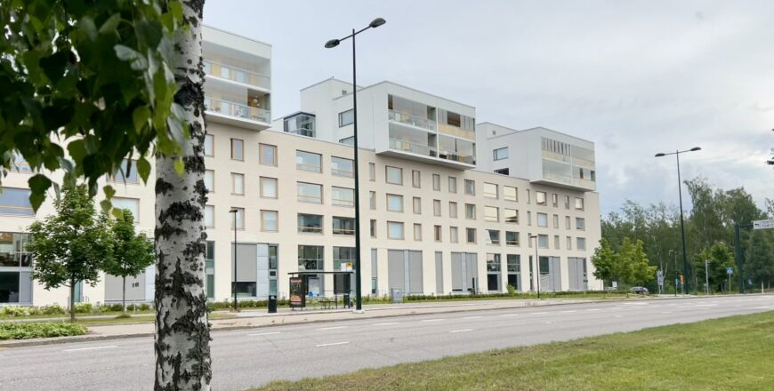 Veritas fastighet på Koltgränden fotograferad från avstånd. På framsidan av byggnaden finns det några träd samt en bilväg och en busshållplats.