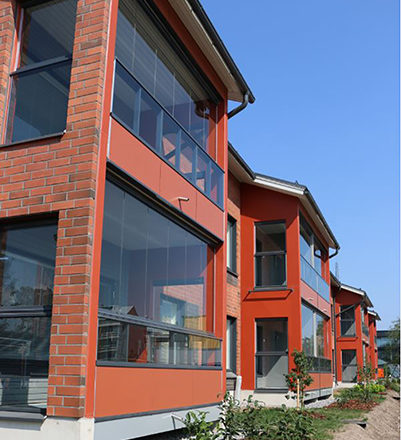 Närbild av Vantaan Kuunliljas inglasade balkonger. Huset är rött och lägenheterna ligger på två våningar.