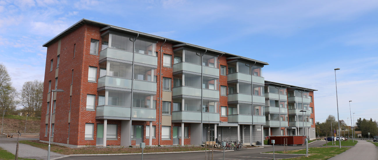 Fasaden på Kehräs gård med elektriska stolpar för bilar, gräsmatta och bred gångväg. Höghuser är av rödbrun tegel och har fyra våningar samt inglasade balkonger, förutom lägenheterna i marknivå.