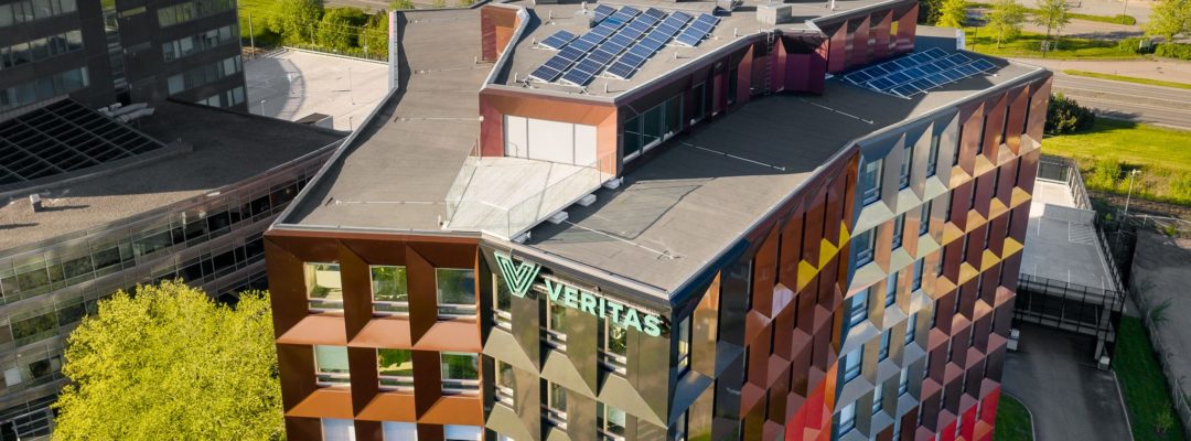 Kesäinen ilmakuva Veritaksen värikkäästä pääkonttorista, Retoriikasta, jonka katolla on kymmeniä aurinkopaneeleja. Taustalla näkyy Helsingin valtatie ja sen takana olevia muita kiinteistöjä.