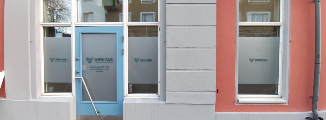 Maarianhaminan konttorin sisäänkäynti kuvattuna ulkopuolelta. Ikkunoissa on teipeissä Veritaksen logot, rakennus on punainen ja harmaa.