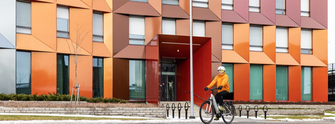 En person cyklar med en elcykel framför Veritas huvudkontor i Åbo. Byggnaden är färggrann och det finns lite snö på marken.